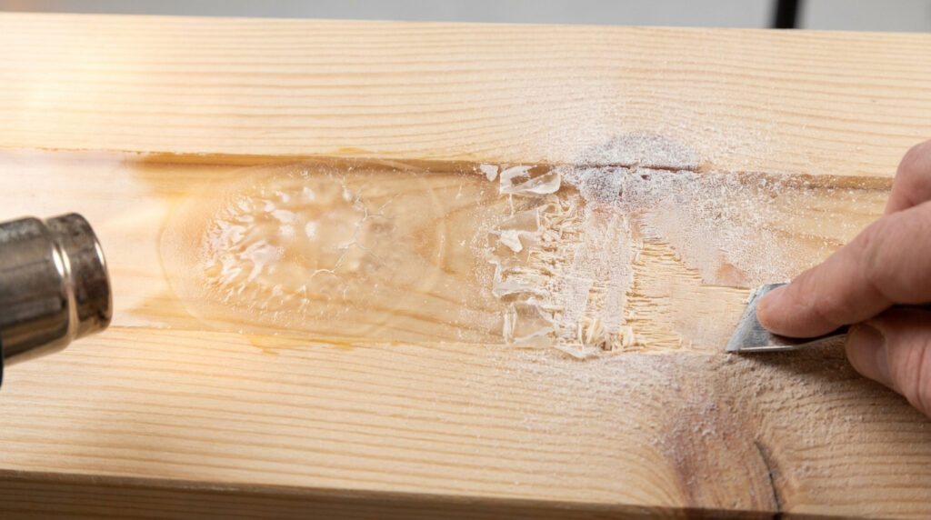 Utilisation d'un pistolet thermique et d'une spatule pour enlever de la résine époxy sur une planche en bois.